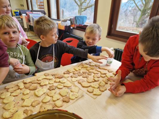 Kinder sitzen an einem Tisch und verzieren frisch gebackene Plätzchen in verschiedenen Formen mit bunten Streuseln
