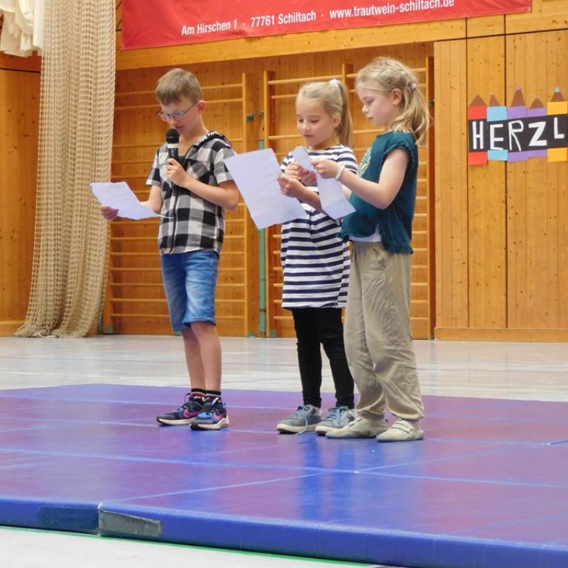 Drei SchülerInnen stehen auf blauen Matten und lesen etwas vor