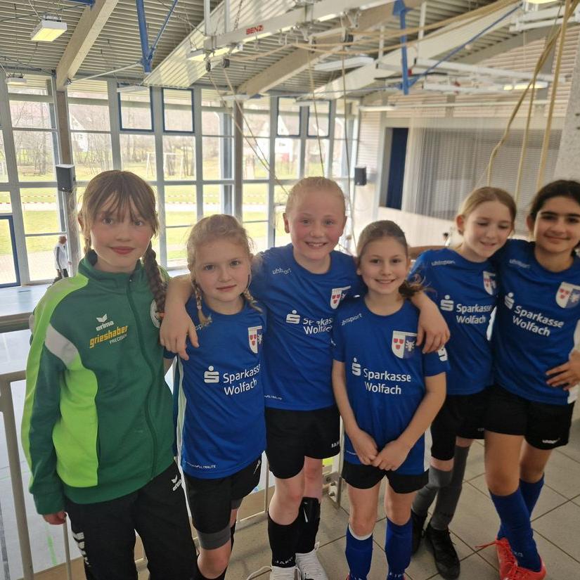 Sechs Mädchen in Fußballtrikots stehen in einer Halle nebeneinander und lächeln in die Kamera