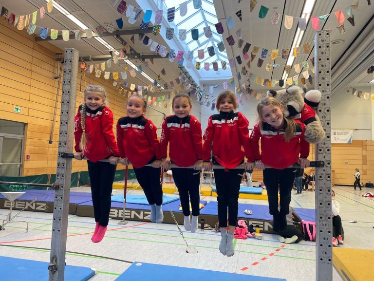 Fünf junge Turnerinnen in Trainigsanzügen stützen sich auf eine Reckstange auf